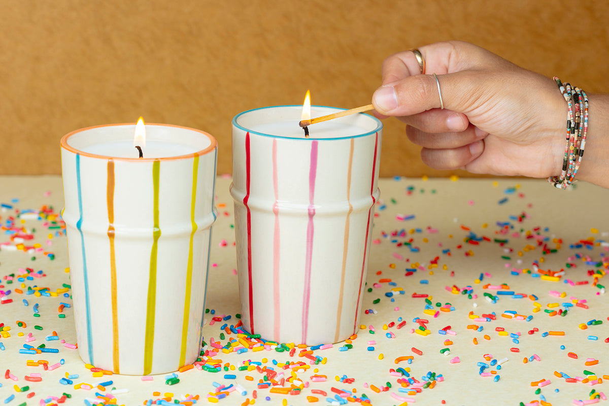 Hand lighting a candle with colorful stripes on a surface covered in confetti.