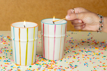 Hand lighting a candle with colorful stripes on a surface covered in confetti.